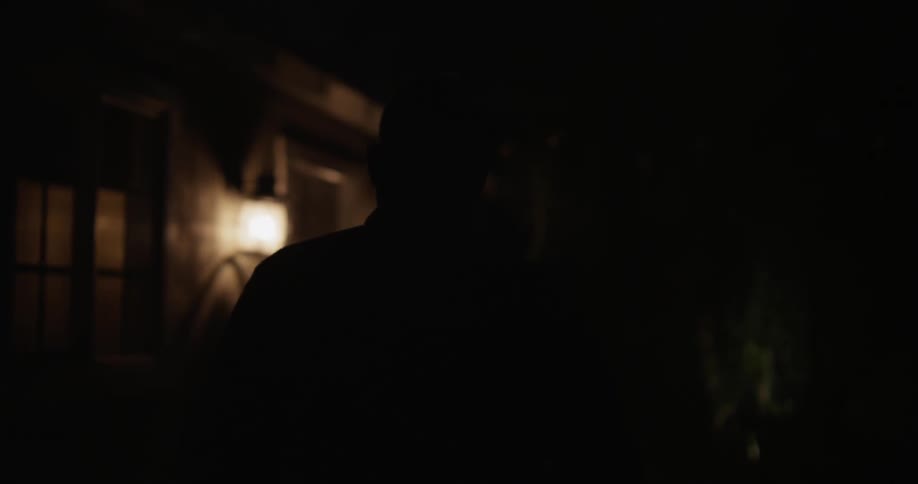 A man approaches a house at night and opens the door