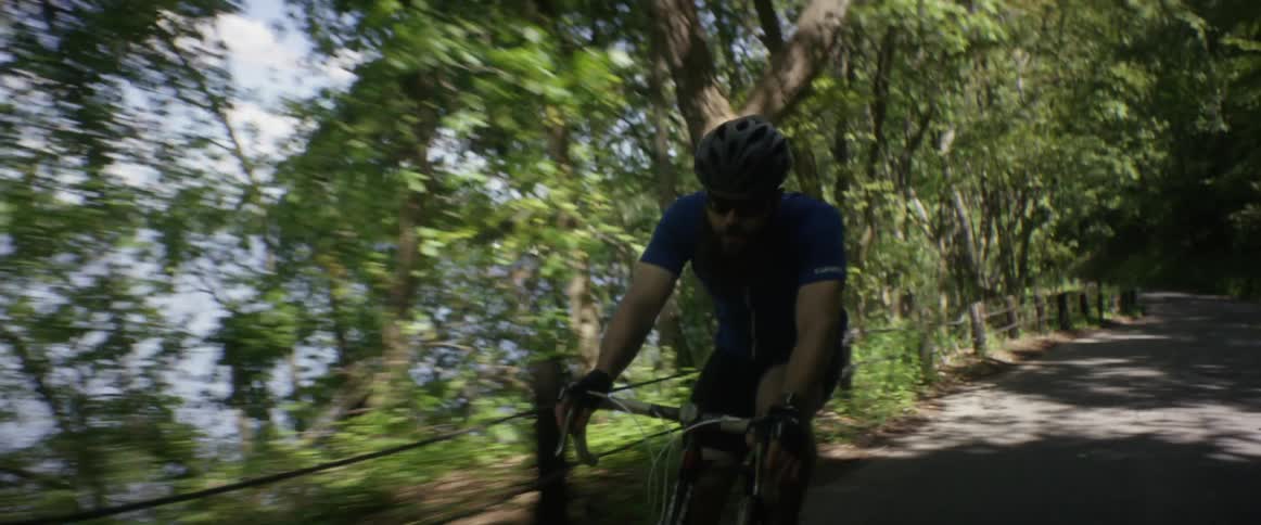 Man cycling down a rural road next to a wooded lake area
