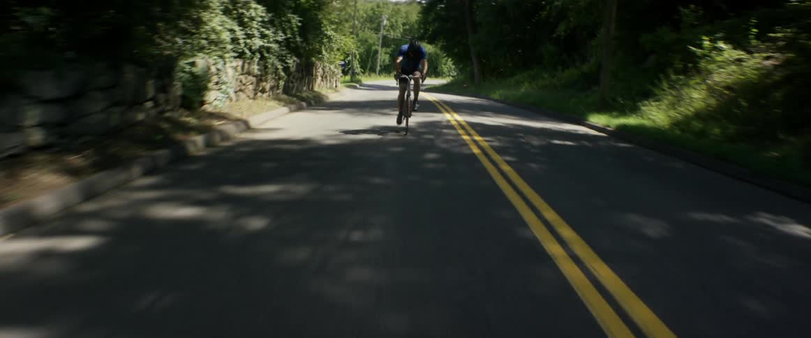 A man riding a racing bicycle quickly down a two lane road