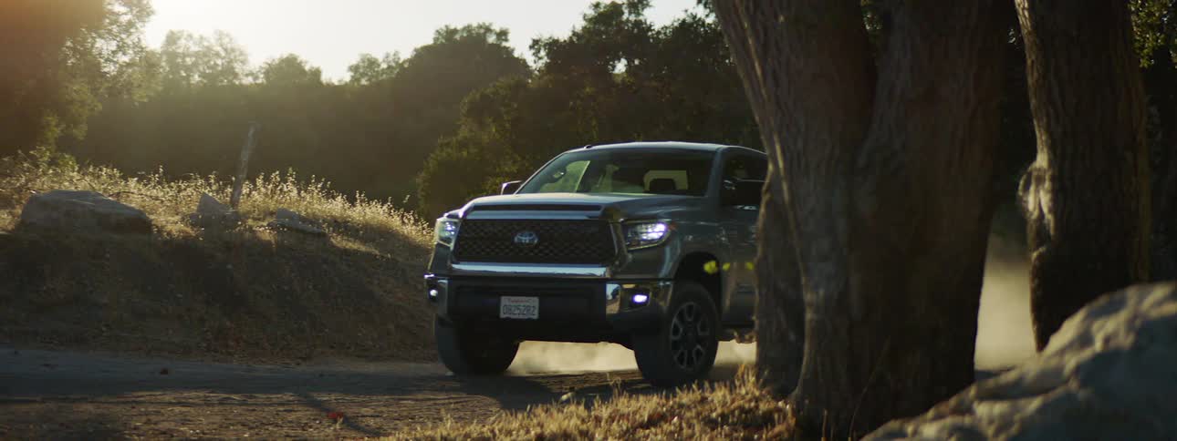 Grey pickup truck drives up on a dirt road at sunset
