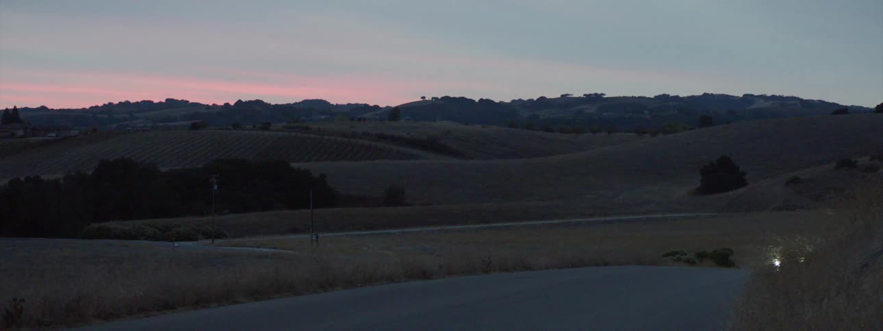 Vehicle driving on the rural road through the hills at sunset