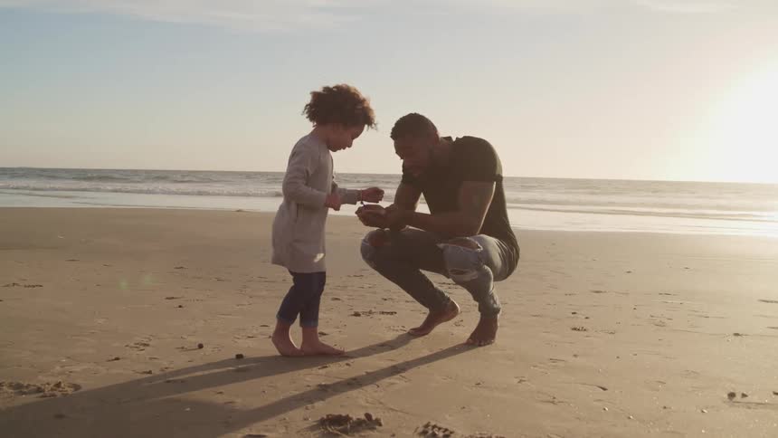 Father and son plays with the sand of the beach next to the ocean at sunset