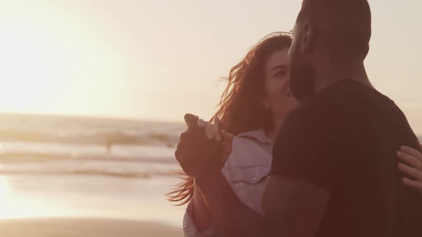 A man and woman romantically dance together beside the ocean water