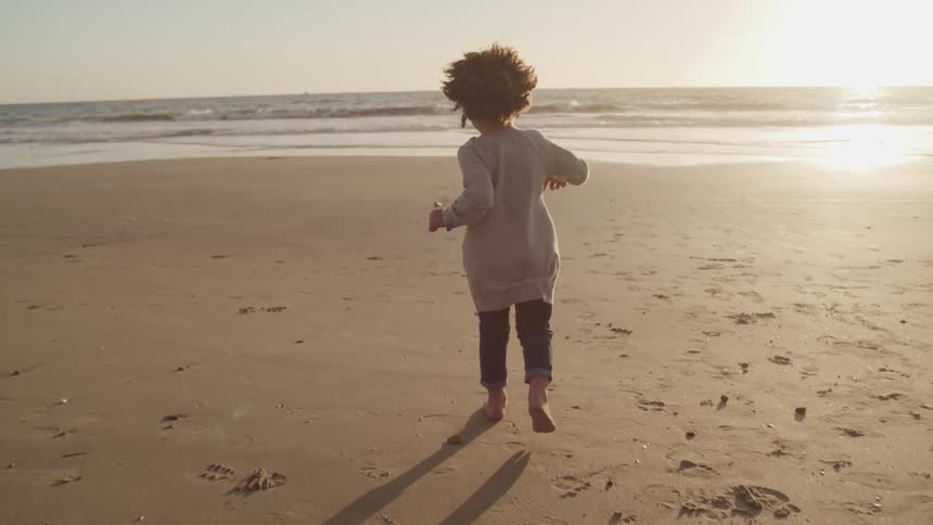 A girl runs barefoot on the wet sand towards the ocean waves