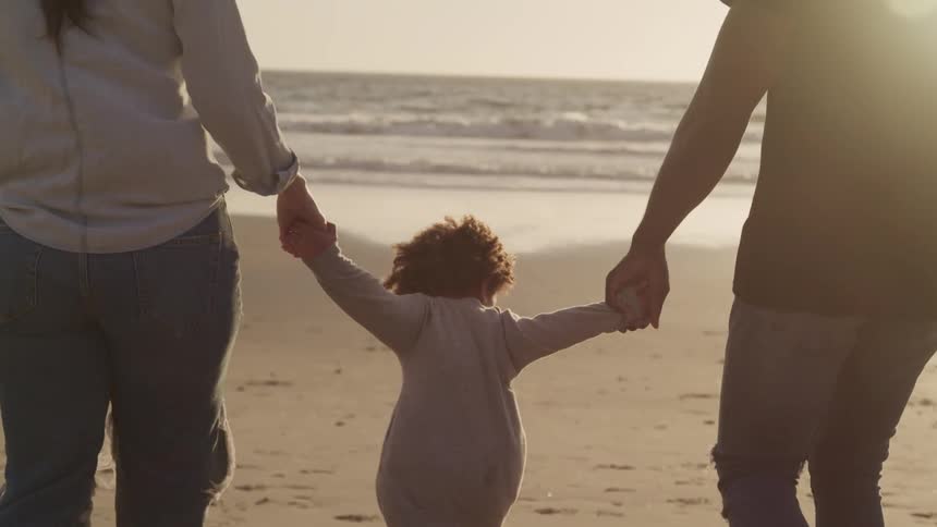 Family walk holding hands on the sands of a beach next to the sea at sunset