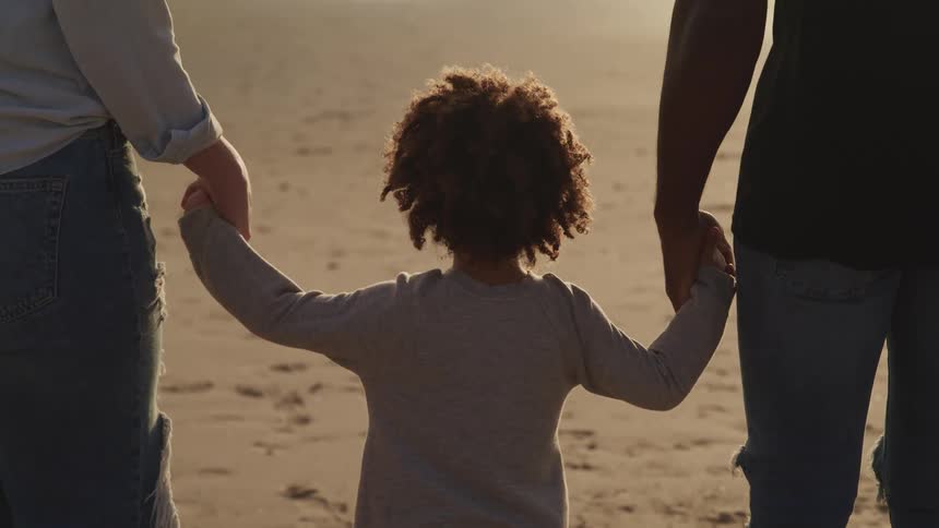 A couple holding hands with a child on the beach