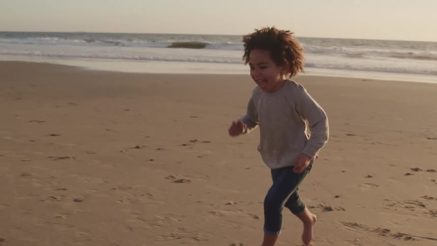 Toddler boy runs barefoot on the sand beach at sunset next to the sea