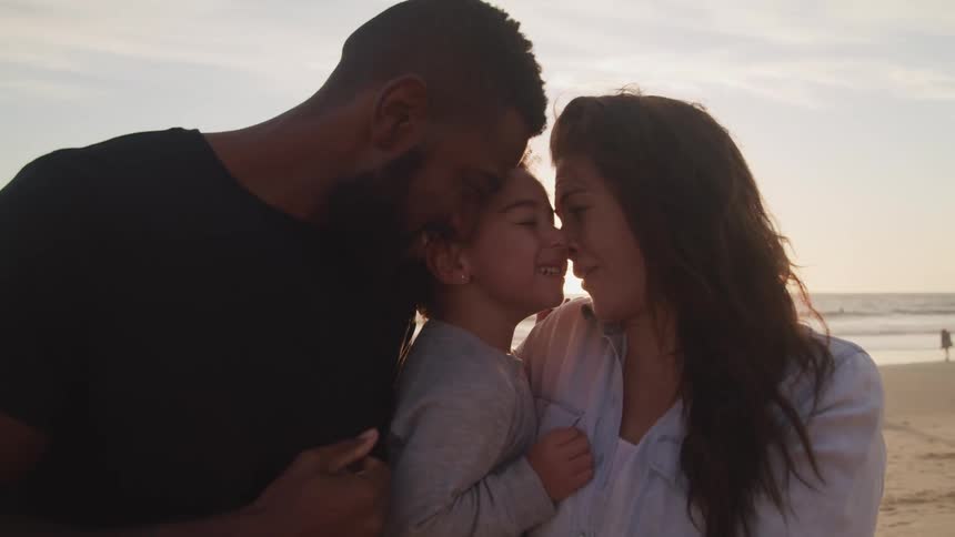 A mother and father hold and hug their son lovingly standing on the beach together
