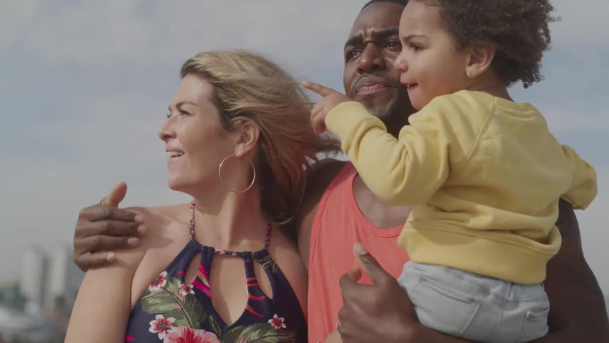 Husband holds child and hugs wife as family smiles and looks around