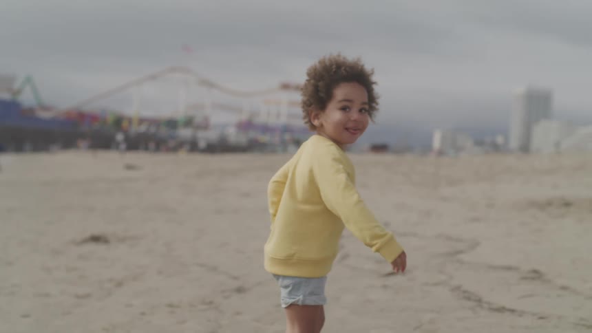 A little boy running on the beach with a ferris wheel a roller coaster and buildings in the background