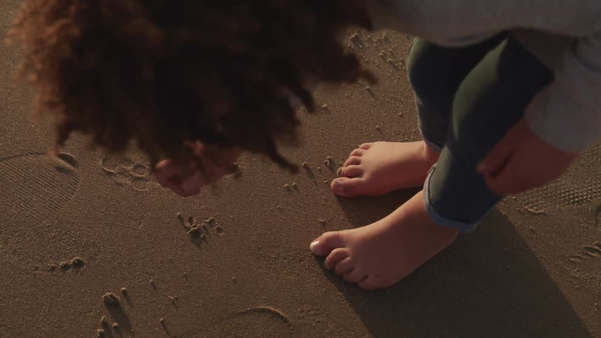 Little barefoot boy plays with the sand on a beach at sunset
