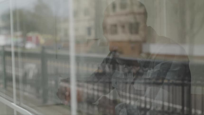 A man sits at a counter by the window in a restaurant and sips on a drink as he watches cars drive by
