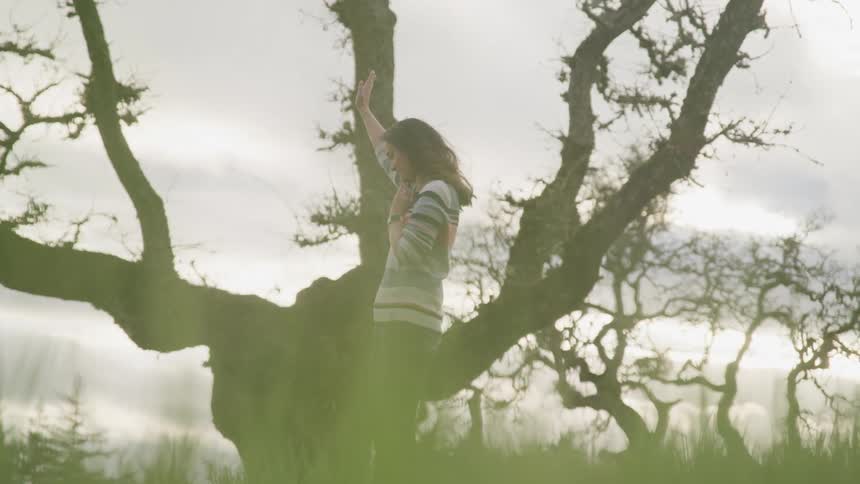 A woman stands next to a tree with her hand in the air