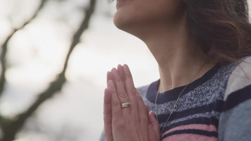 Woman stands outside under tree praying