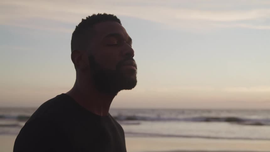 A man standing on the beach with his eyes close with the sky and clouds in the background