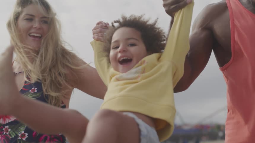 A mother and father swing their daughter by the arms as they walk along the beach