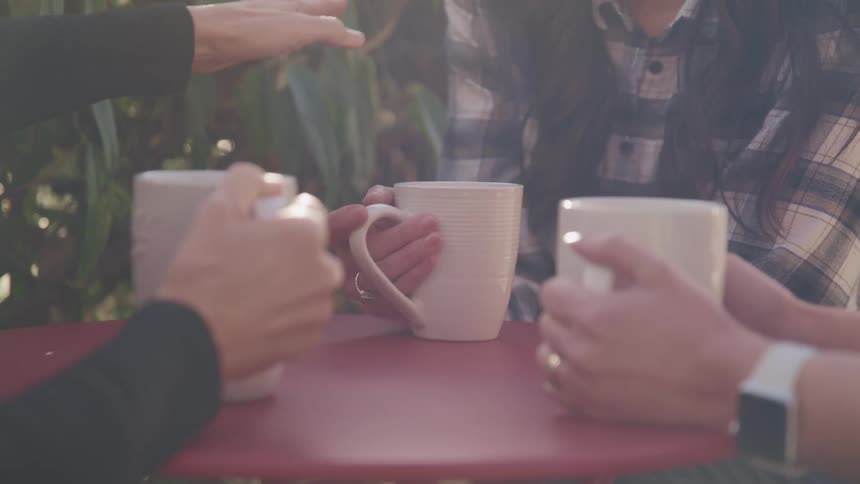Three people sit at an outdoor table with coffee mugs