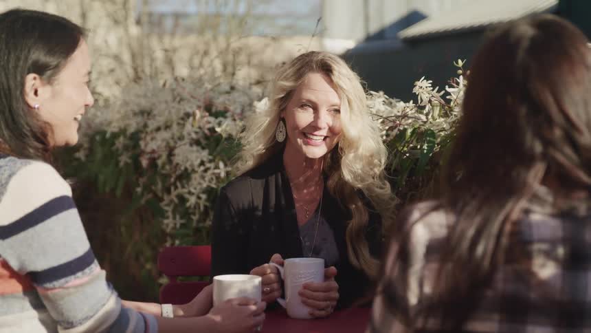 A group of women sitting at a table drink coffee and talk to each other in a garden