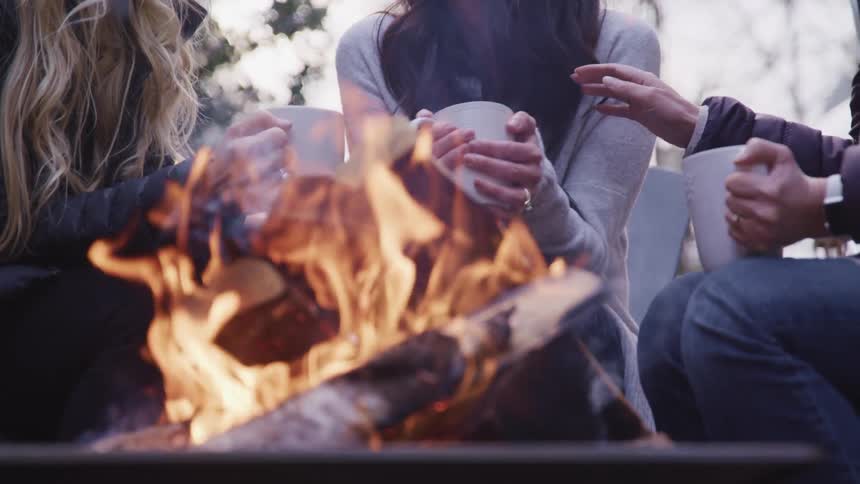 Three women drink at a campfire