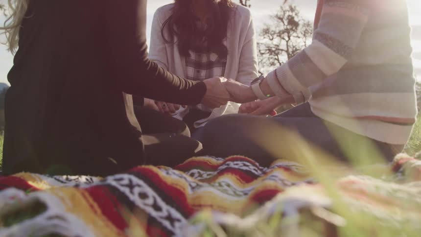 Three friends sit outside and hold hands