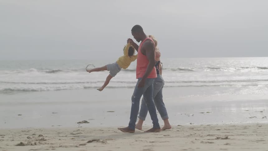 Family walk holding hand playfully on the shoreline of a beach at sunset