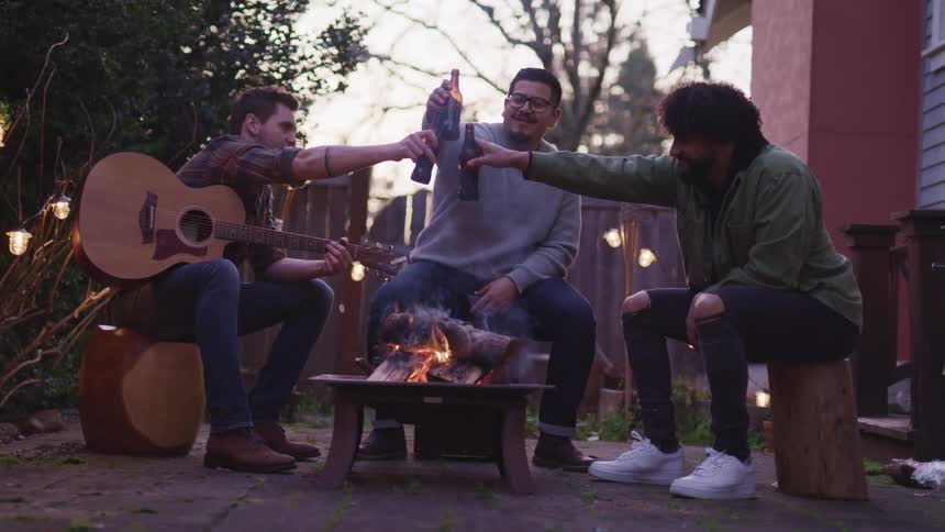 Three men toast beers at a campfire