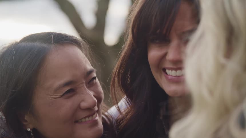 Women stand outdoors smiling and hugging