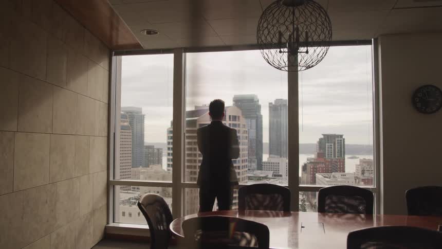 Man wearing a suit looks at the city skyline from the window of a meeting room in the office