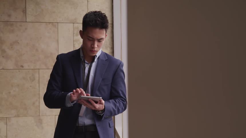 Man stands in a hallway and scrolls on a tablet