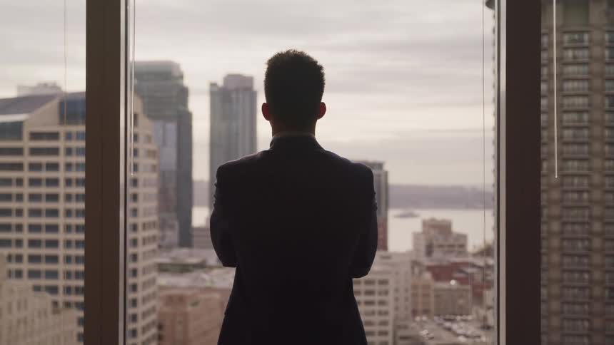 A man is standing in an office building and looking out a window