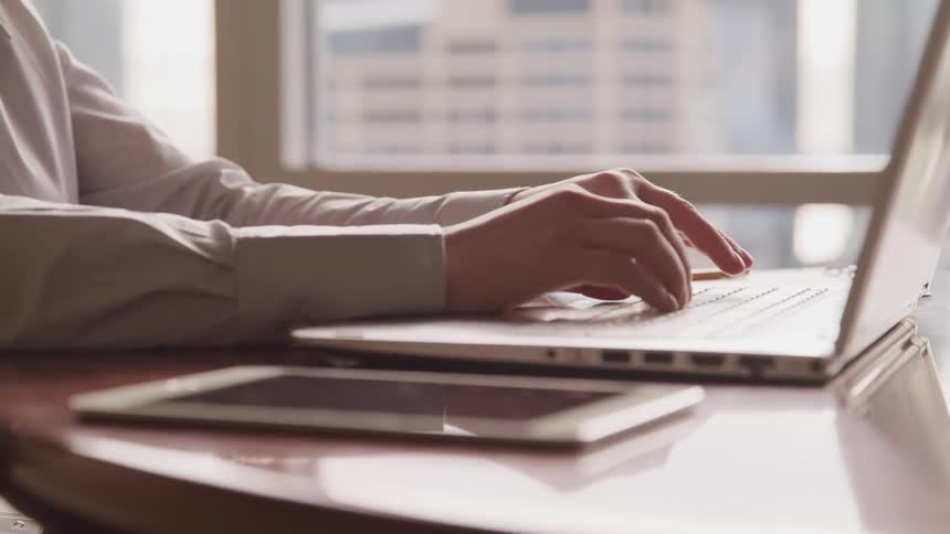Woman types on a laptop as a tablet lays nearby