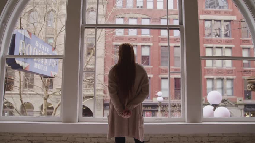 A woman stands in front of an arched window in a hotel and looks at the buildings across the street