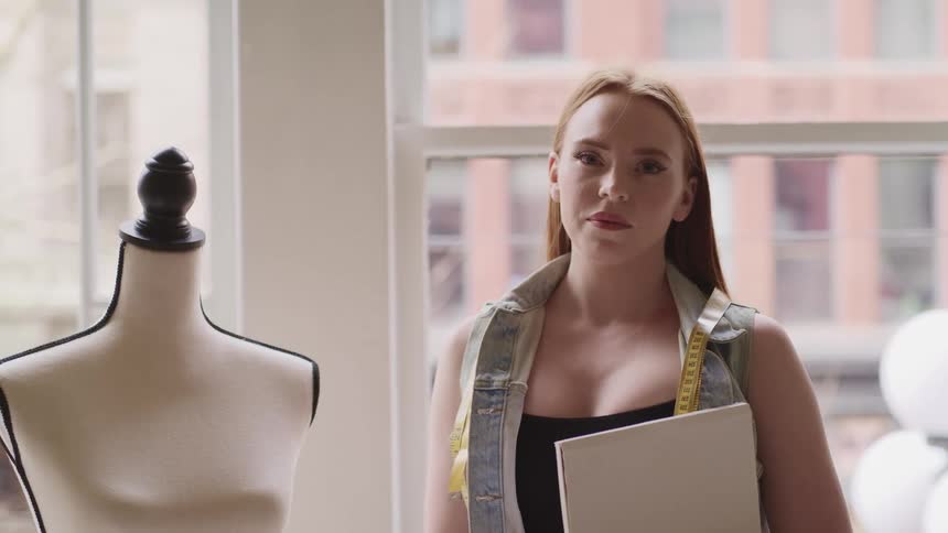 A woman with a tape measure around her neck stands next to a mannequin