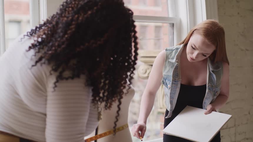 Two women measure a mannequin