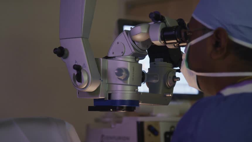 A doctor with scrubs and a mask looking into a microscope in a clinic