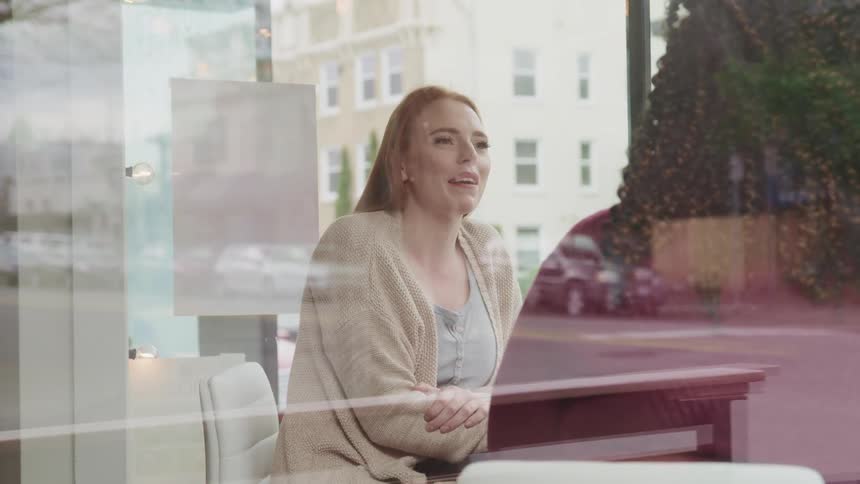 A pair of women chat and laugh while sitting near large windows