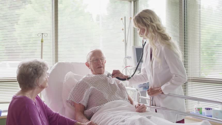 An elderly make in a hospital bed being treated by a female doctor in a hospital