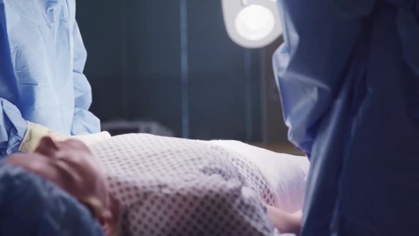 Medical team of surgeons in hospital doing surgical intervention on a young woman lying on operating table