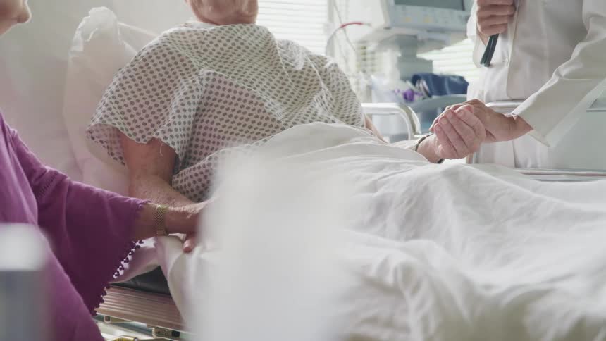 A doctor and woman holds hands with a patient in bed