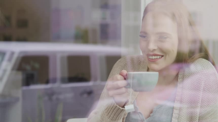 Woman with red hair sitting at a table drinks a cup of tea and smiles in a cafe