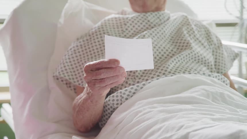Doctor gives a note to an elderly patient laying in a hospital bed