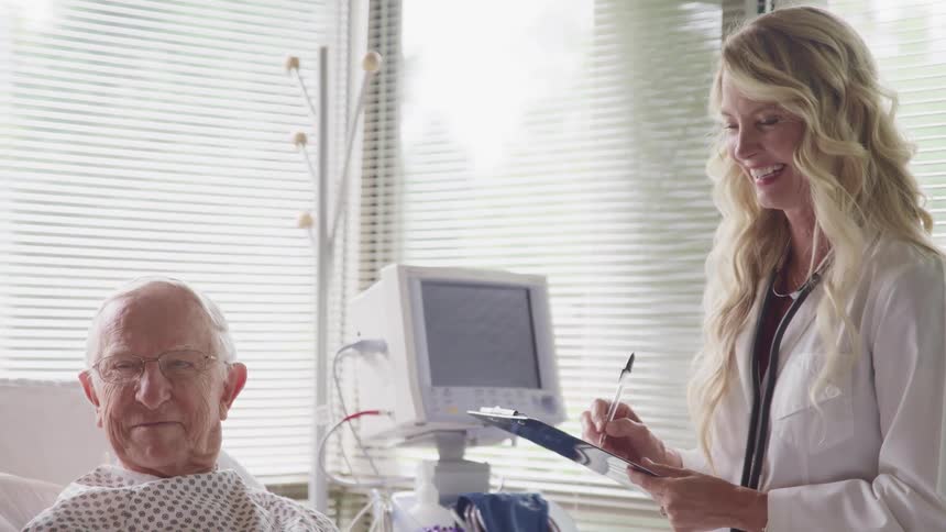 A doctor stands at a patients bed holding a chart and talks and laughs