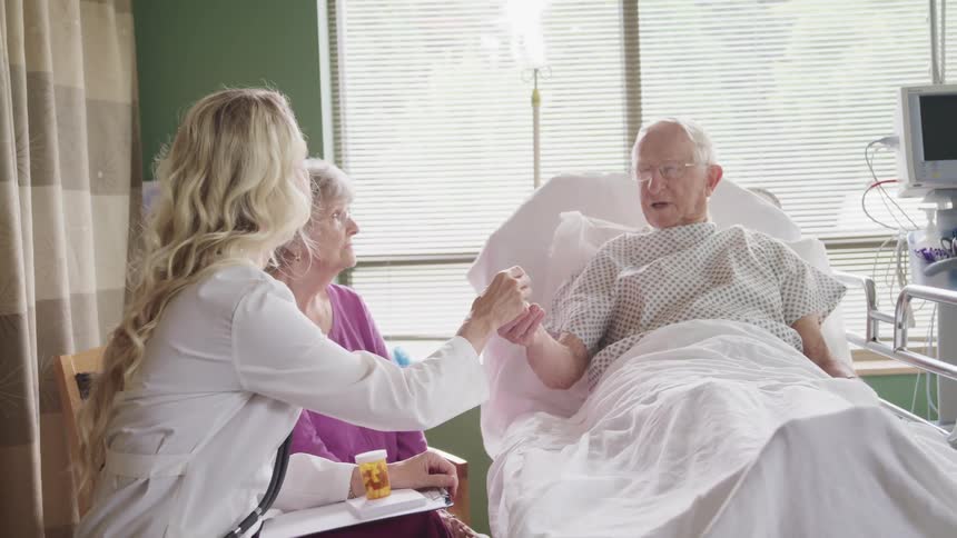 Doctor sitting next to patients wife hands the male patient a prescription bottle containing medication while having a consultation with him