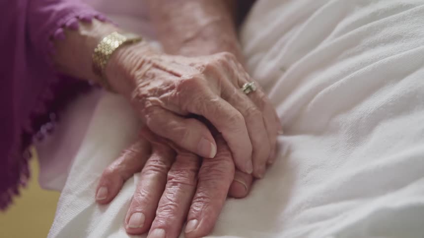 Two people hold hands by a bed