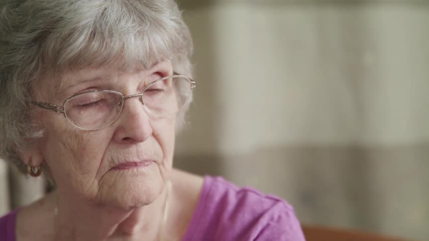 An elderly woman turns her head to look at something and closes her eyes and then opens them