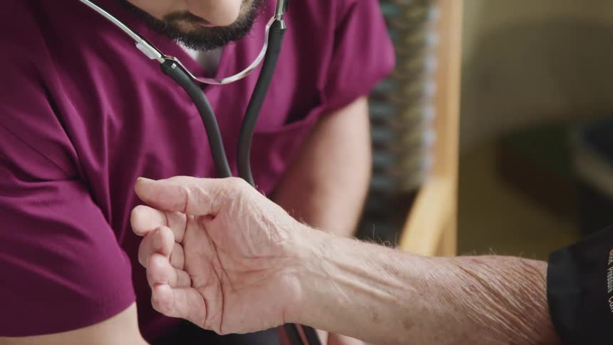 A male nurse listens to a patients heart while checking his blood pressure