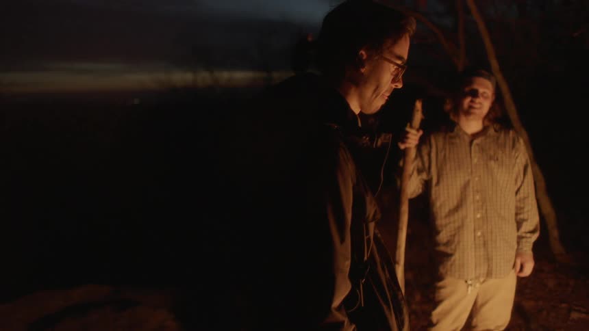 Two men looking into a campfire
