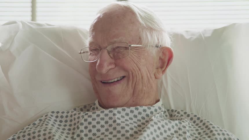 An elderly male laying in a hospital bed smiling