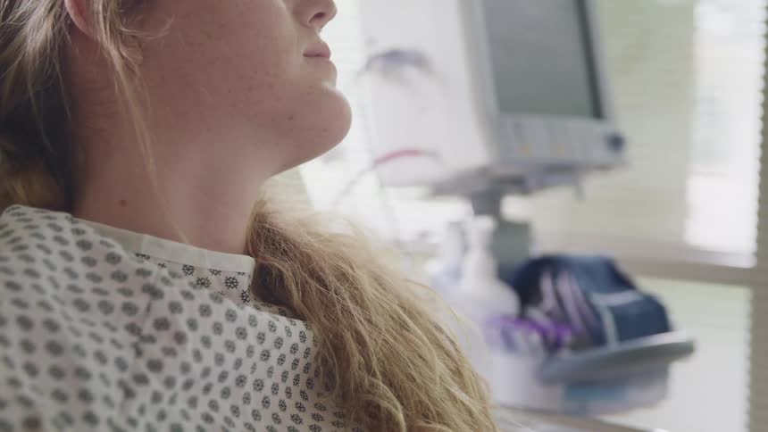 A woman with a hospital gown laying in a hospital bed with a window in the background