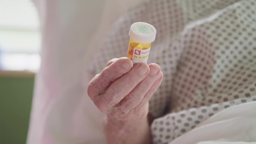 An elderly patient in a hospital bed holding a prescription bottle